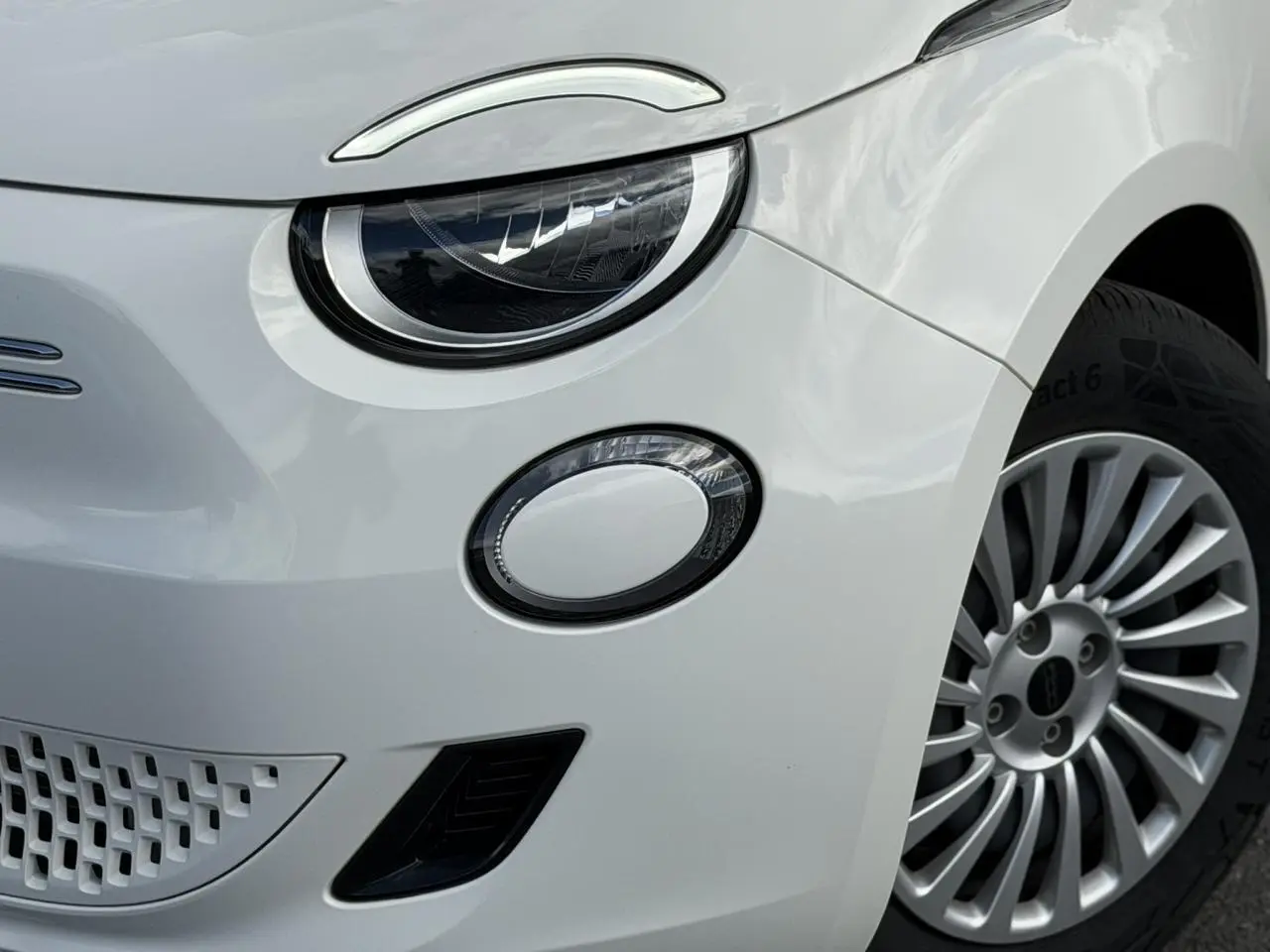 Gros plan sur l'avant droit blanc Artic du FIAT 500 électrique, mettant en valeur le phare rond et la jante alliage.