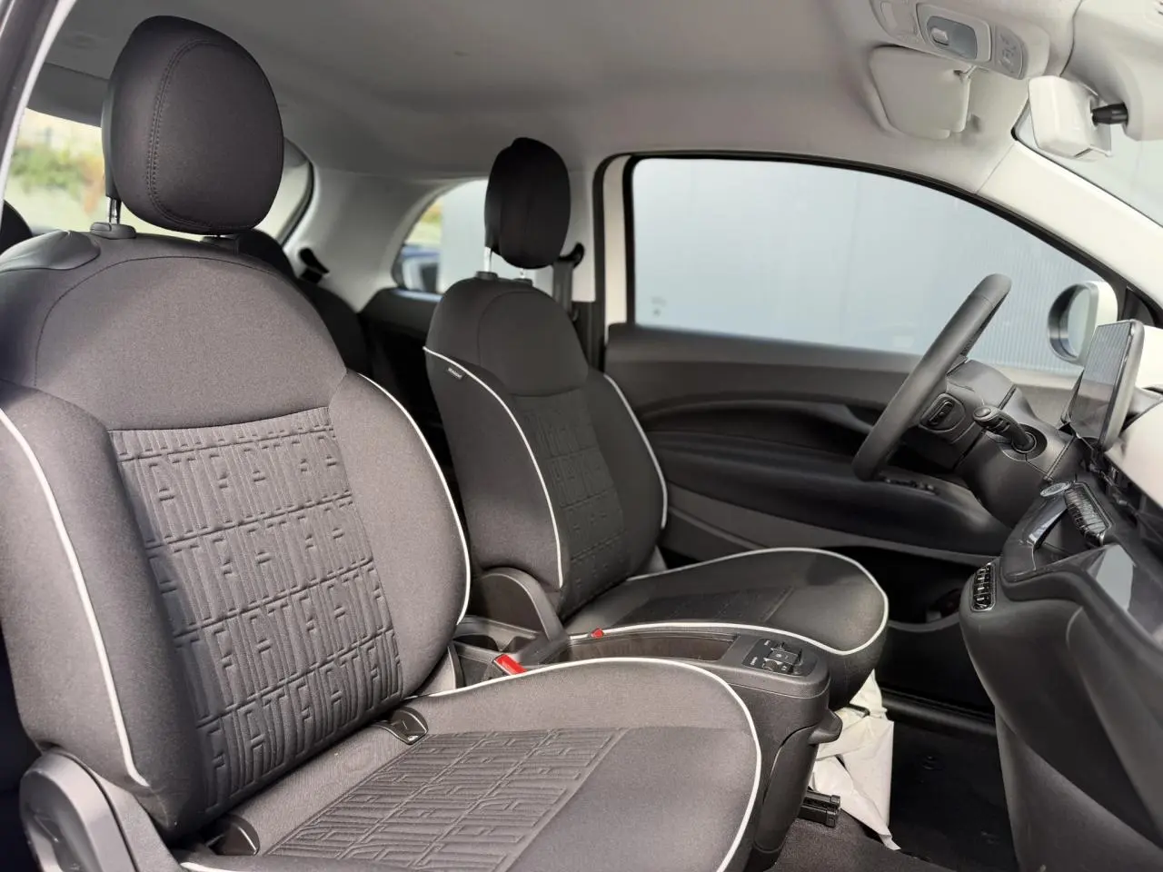 Vue intérieure côté droit de la Fiat 500 électrique 2024, sièges tissu noir avec surpiqûres blanches et planche de bord noire.