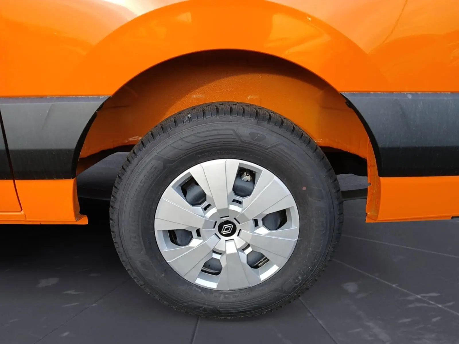 Gros plan sur la roue arrière droite d’un Renault Master orange, avec jante argentée et pneu tous temps visible.