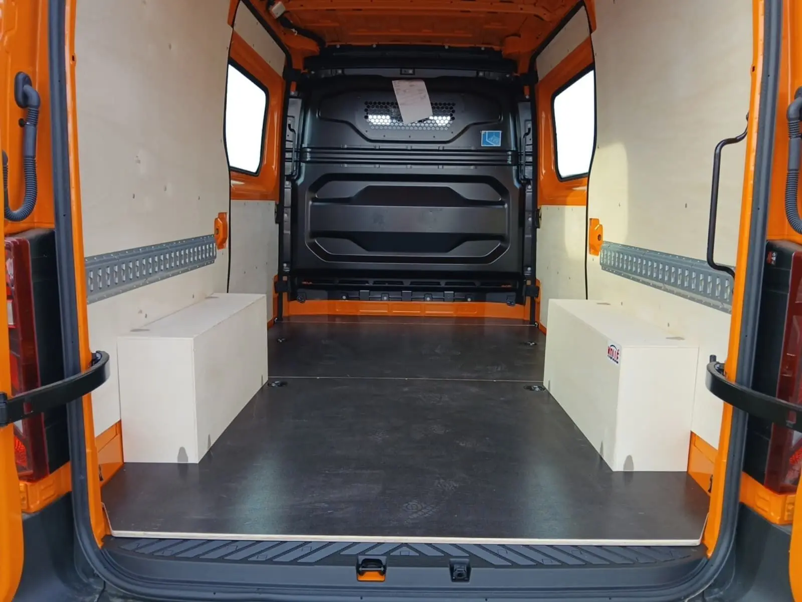 Vue arrière intérieure du Renault Master orange L2H2, montrant l’espace de chargement avec panneaux bois et sol noir.