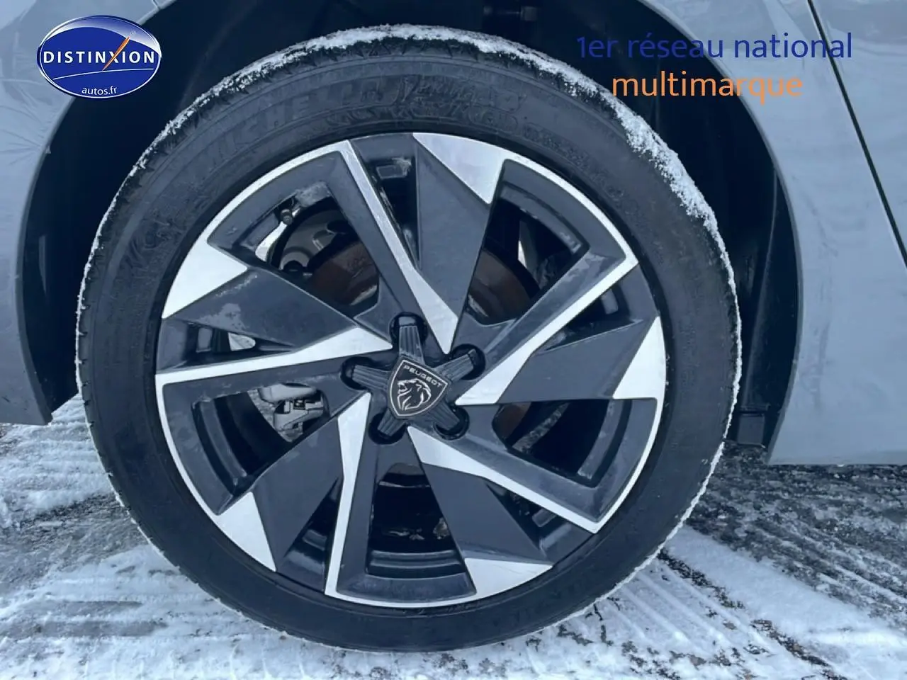 Gros plan sur la jante alu noire et argentée d'une Peugeot 308 gris sélénite, avec logo lion au centre, sur sol enneigé.