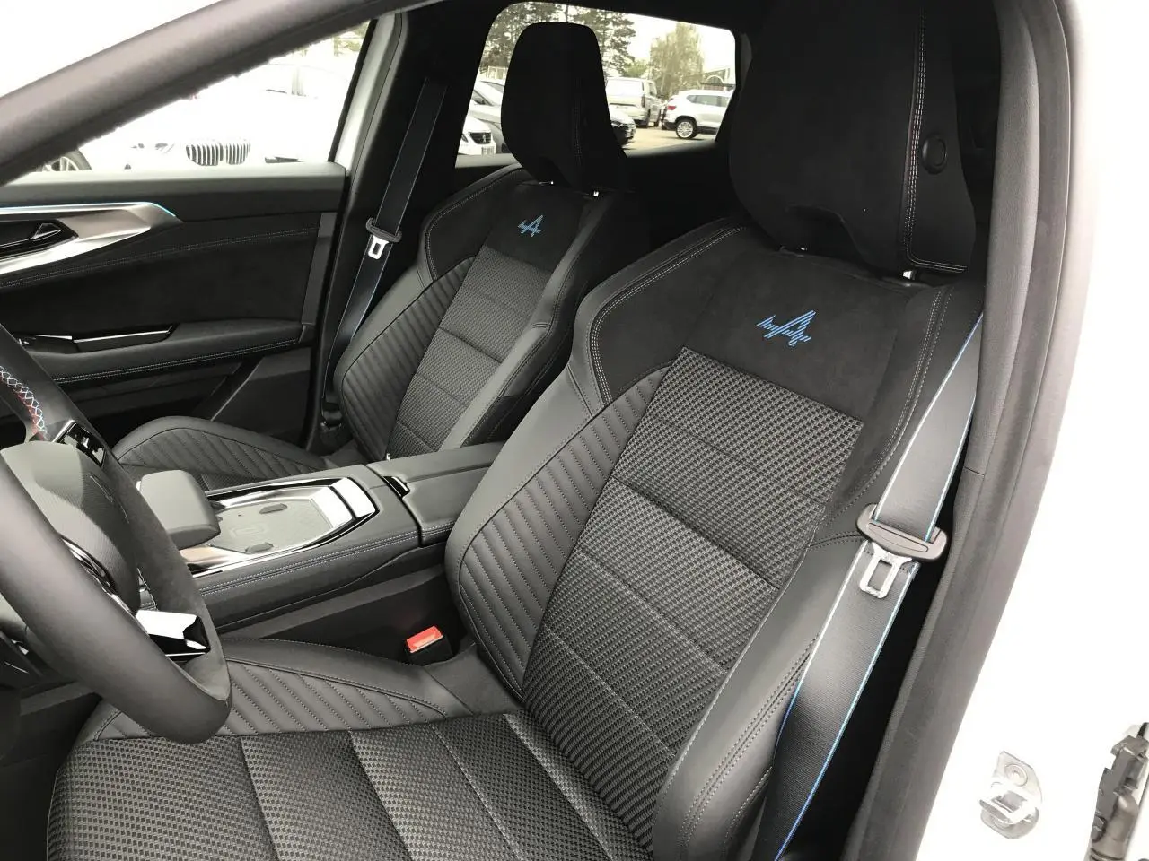 Vue intérieure côté conducteur du Renault Austral blanc, sièges sport noirs avec logo Alpine bleu brodé.