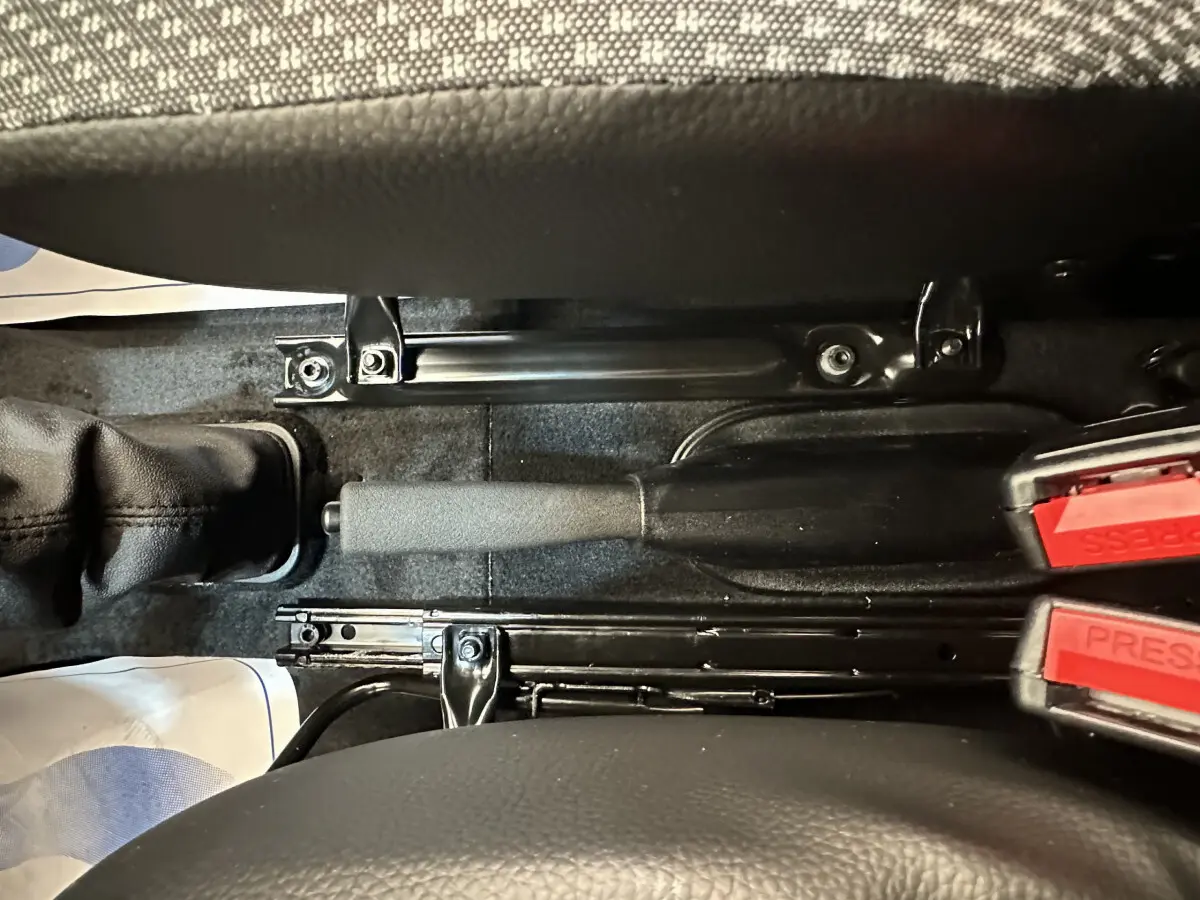 Gros plan intérieur sur le frein à main et les ceintures de sécurité rouges entre les sièges d'une Aixam Ambition E City Pack blanche.