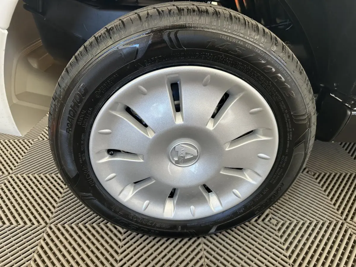 Gros plan sur la roue avant droite d'une Aixam Ambition E City Pack blanche avec enjoliveur argenté et logo central.