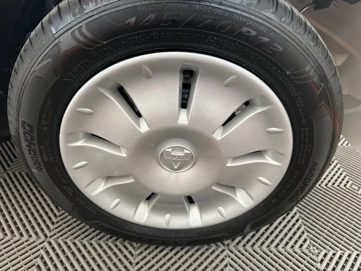 Gros plan sur la roue avant droite d'une Aixam Ambition E City Pack blanche avec jante argentée et logo central.