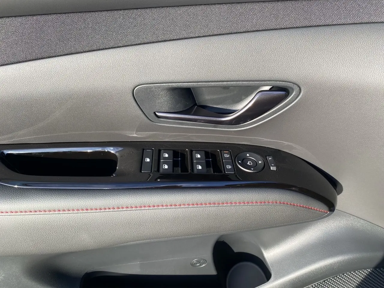 Gros plan sur la porte côté gauche du Hyundai Tucson 2025 noir avec commandes de vitres et poignée intérieure.