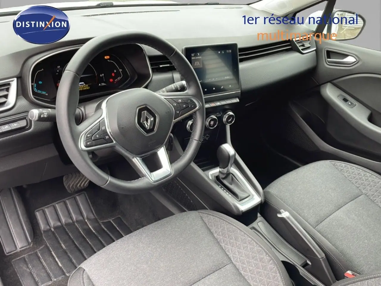 Vue intérieure centrée sur le volant et la console centrale d'une Renault Clio 2020, sièges tissu gris et tableau de bord noir.