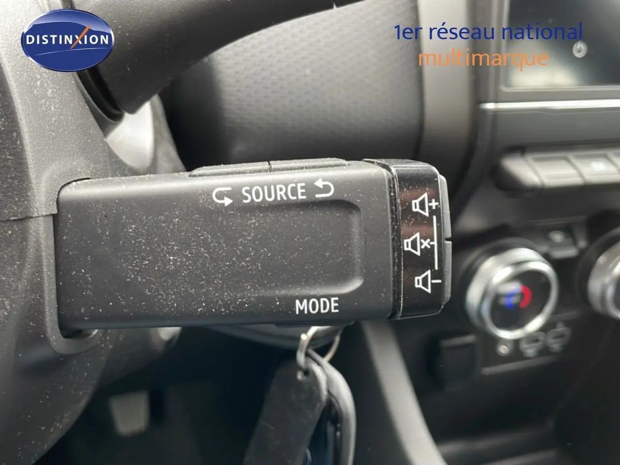 Gros plan sur la commande au volant de la Renault Clio blanche, avec boutons source et mode visibles dans l'habitacle.