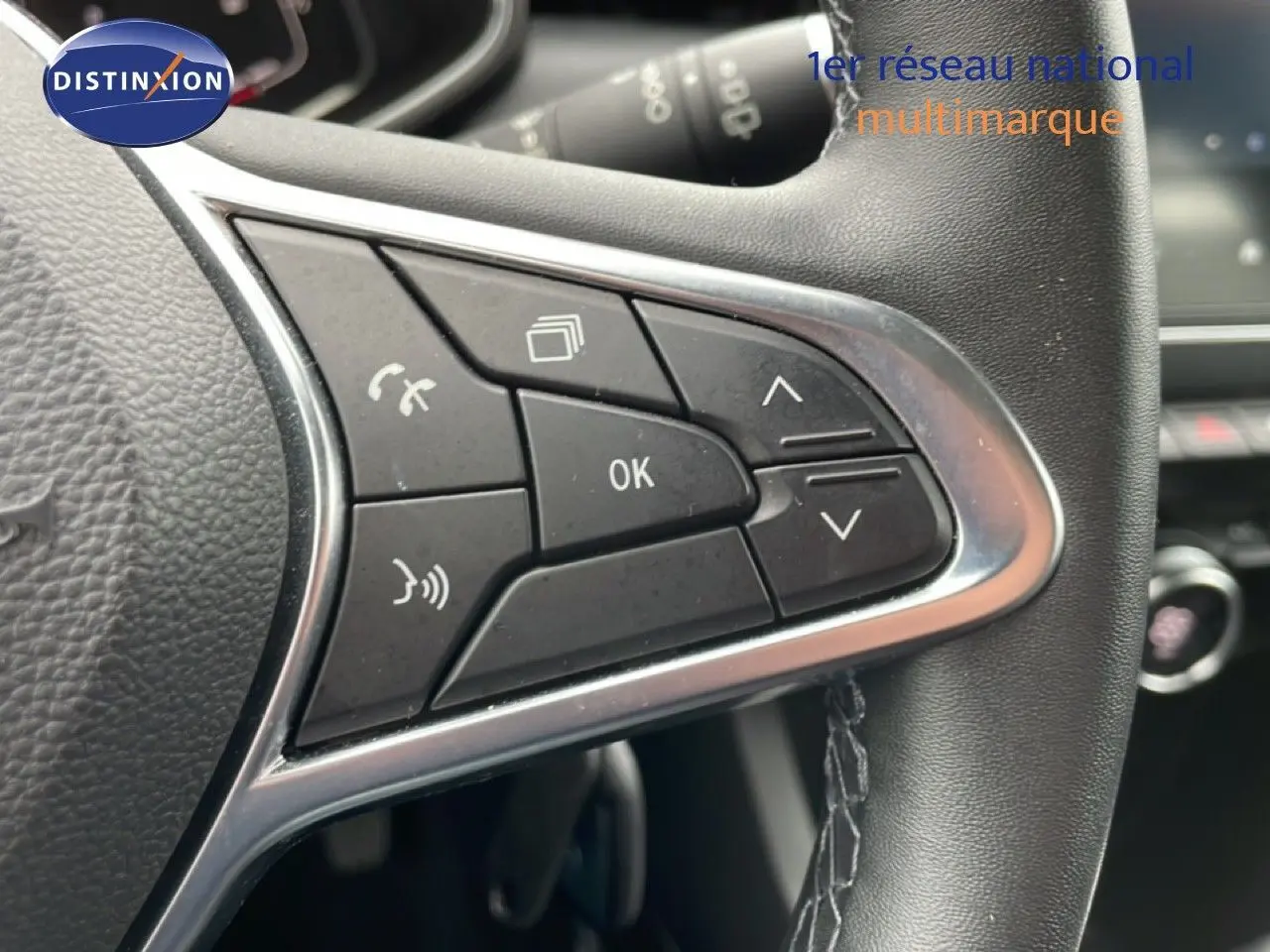 Gros plan sur les commandes multifonctions à gauche du volant cuir noir de la Renault Clio V 1.6 E-TECH blanche.