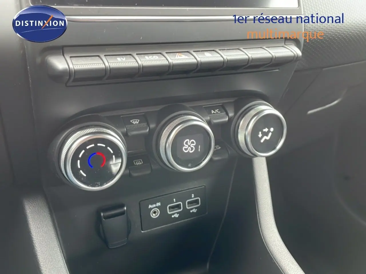 Gros plan sur les commandes de climatisation et les ports USB d’une Renault Clio blanche Glacier, vue intérieure frontale.