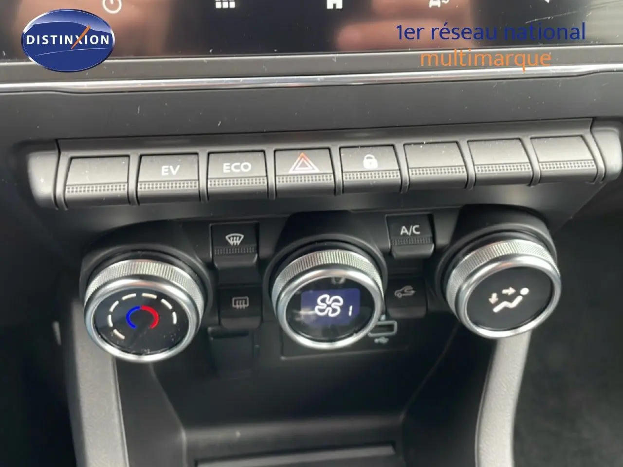 Gros plan sur la console centrale de la Renault Clio blanche, montrant les commandes de climatisation et les boutons de fonction.