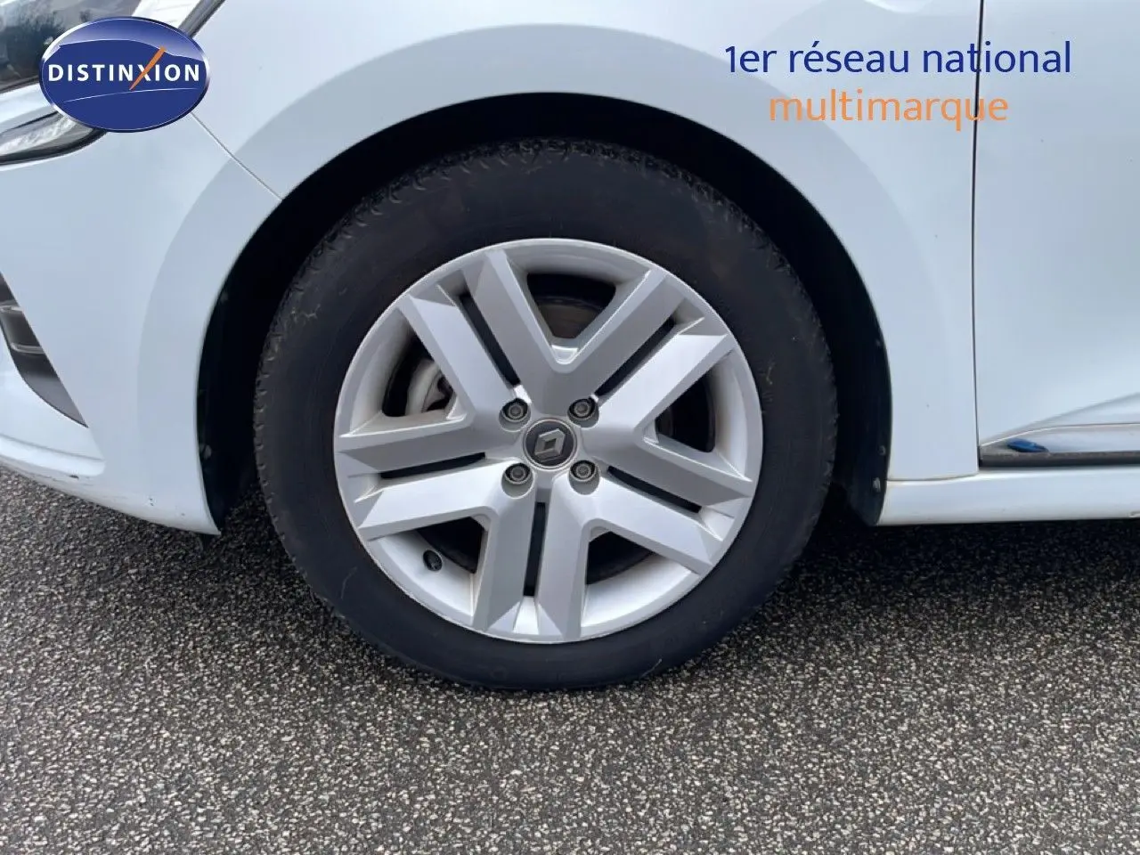 Gros plan sur la roue avant gauche d'une Renault Clio blanc glacier, mettant en valeur la jante alliage distinctive.