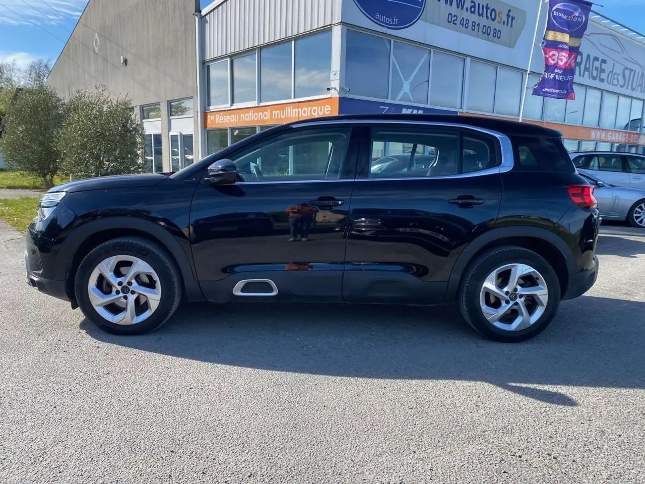 Vue de profil côté gauche d'un Citroën C5 Aircross noir avec jantes alliage 18 pouces, stationné devant un bâtiment.