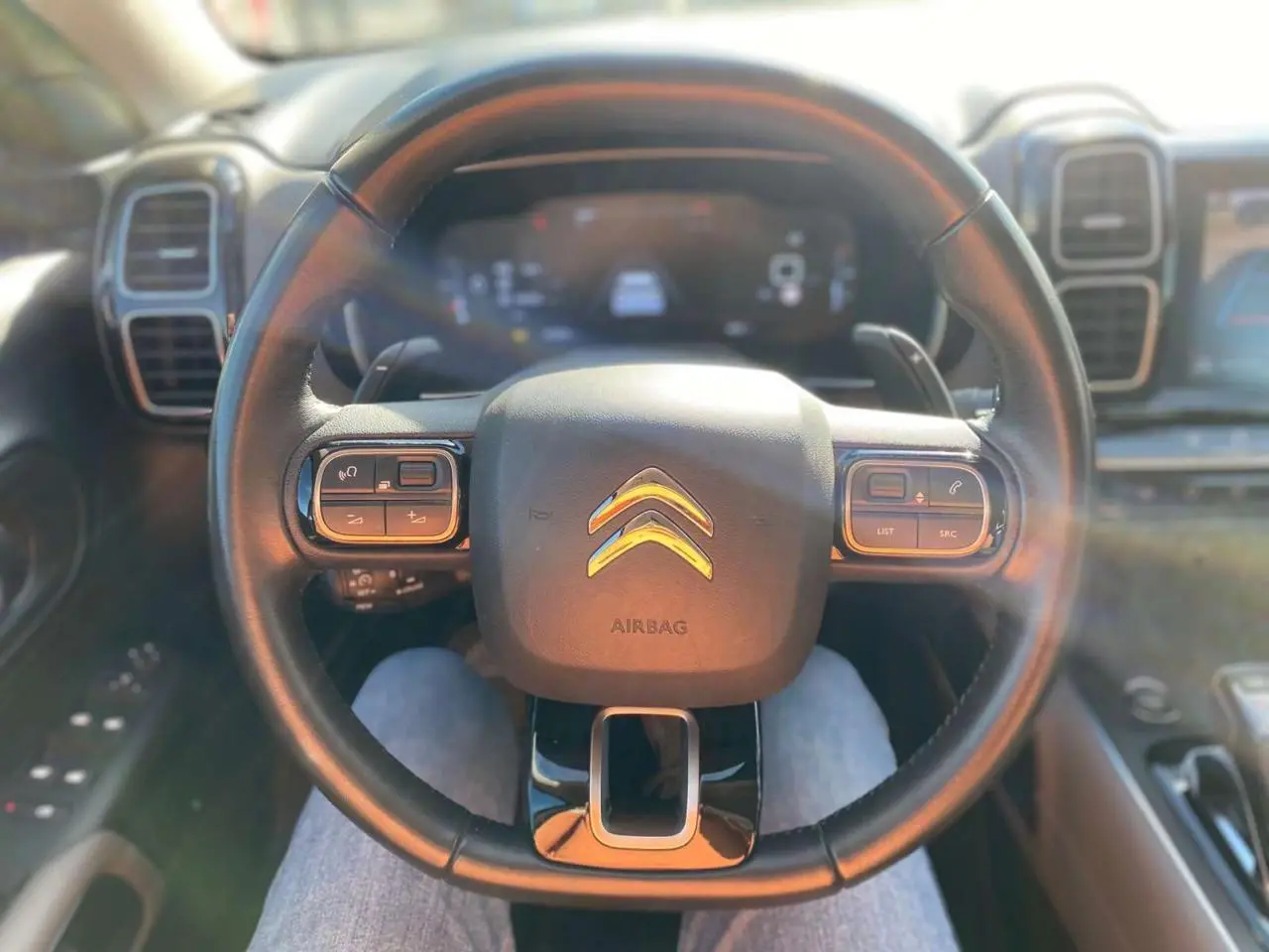 Vue rapprochée du volant noir du Citroën C5 Aircross 2021 avec commandes intégrées et tableau de bord numérique flou.