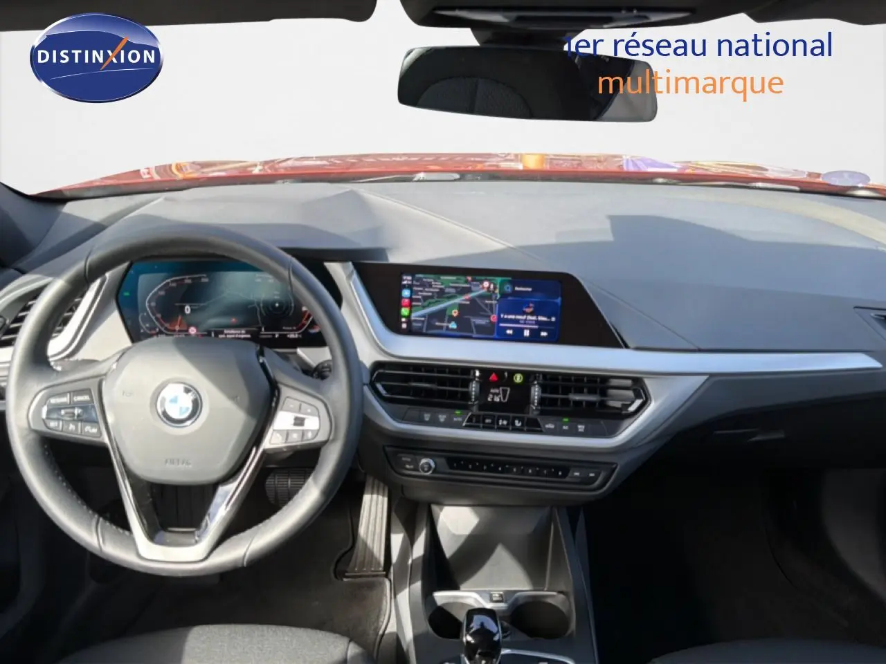 Vue intérieure avant de la BMW Série 1 116i 2022, tableau de bord moderne avec écran central et volant multifonction noir.