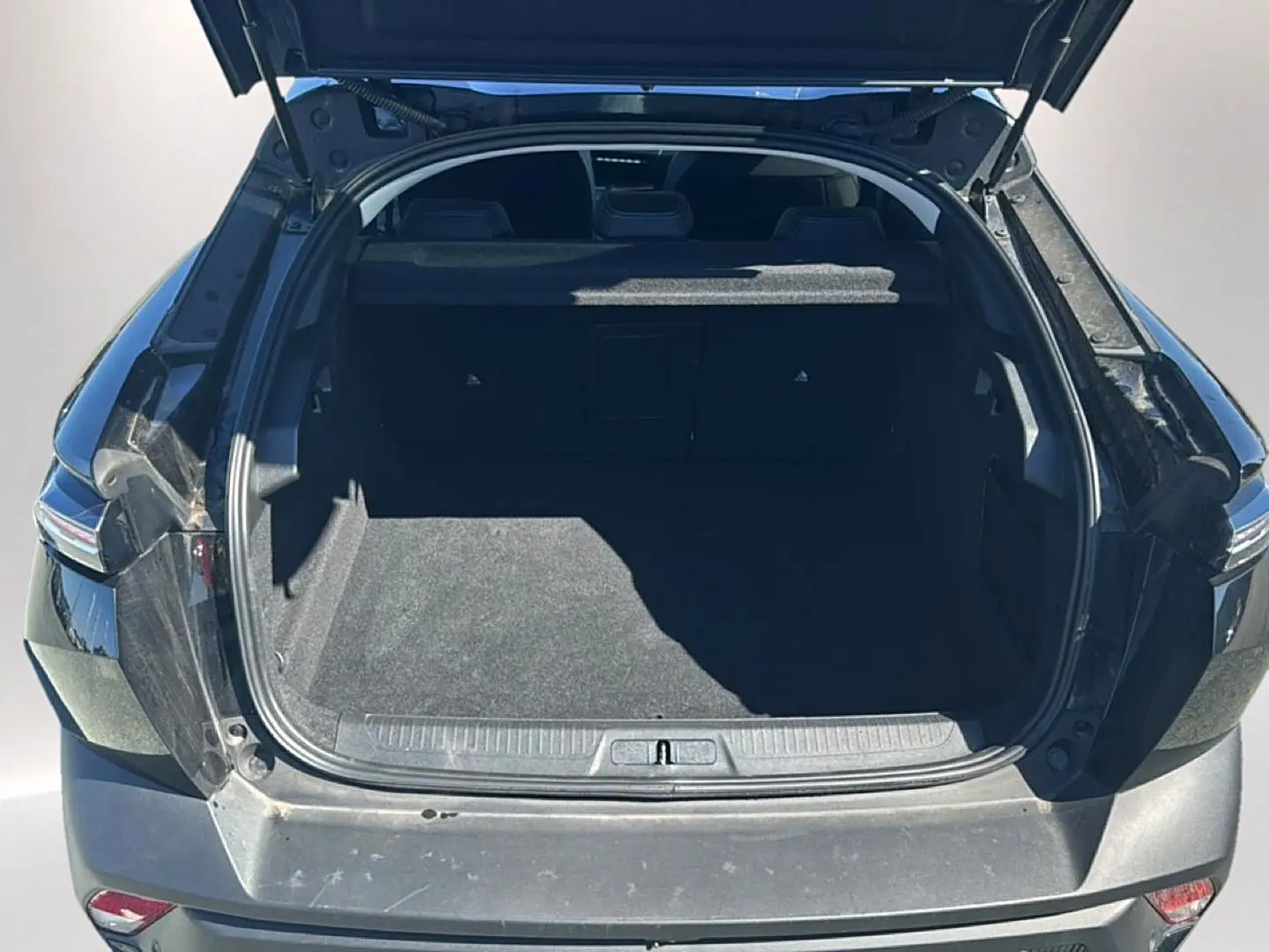 Coffre ouvert vu de l'arrière d'une Peugeot 408 Hybrid 145 allure e-dcs6 noire, montrant l'espace de chargement vide.