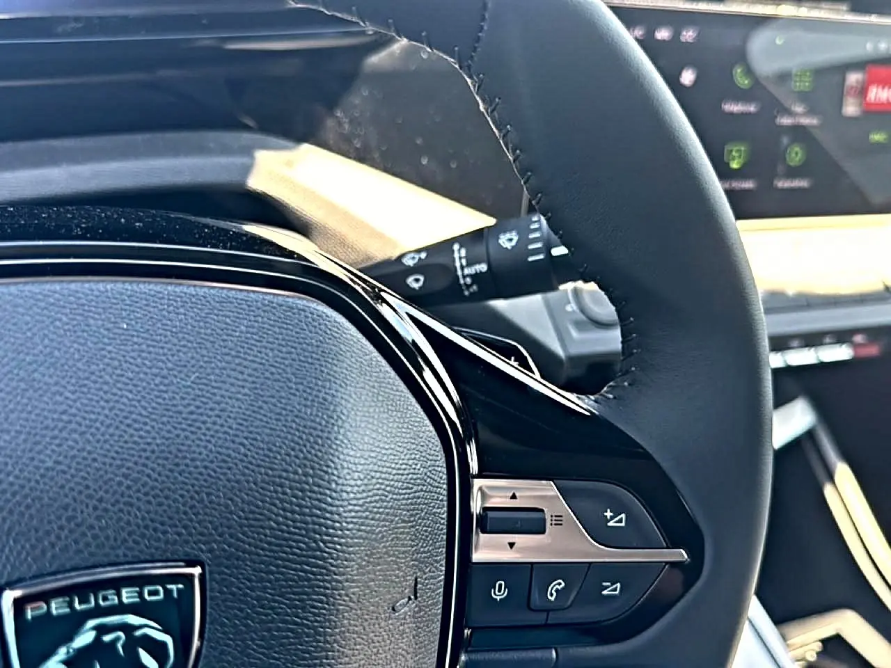 Gros plan sur le volant cuir noir de la Peugeot 408 Hybrid 145 allure, avec commandes audio et téléphone intégrées.