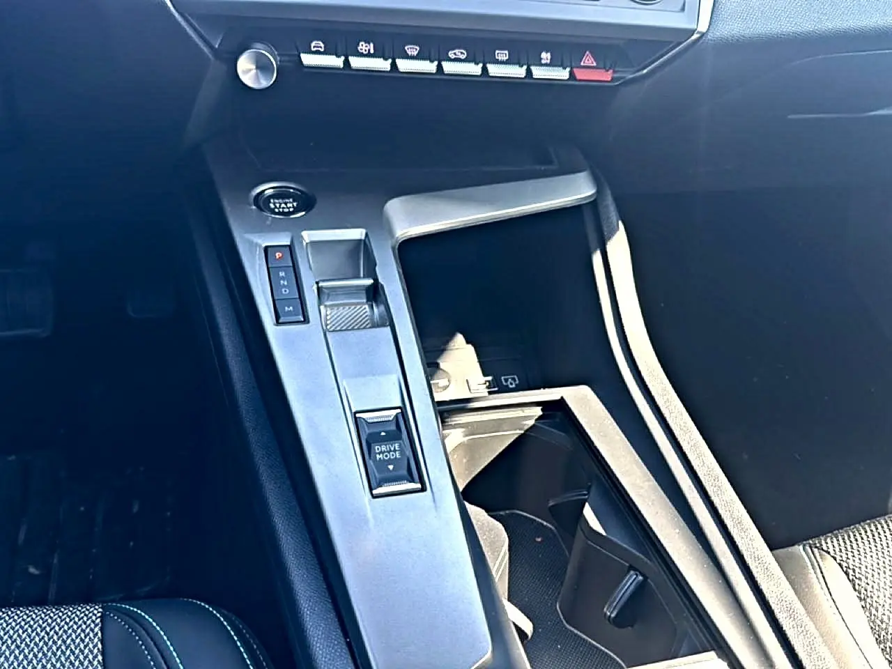 Vue intérieure centrée sur la console centrale noire du Peugeot 408 Hybrid 145 allure avec sélecteur de boîte auto et bouton Drive Mode.