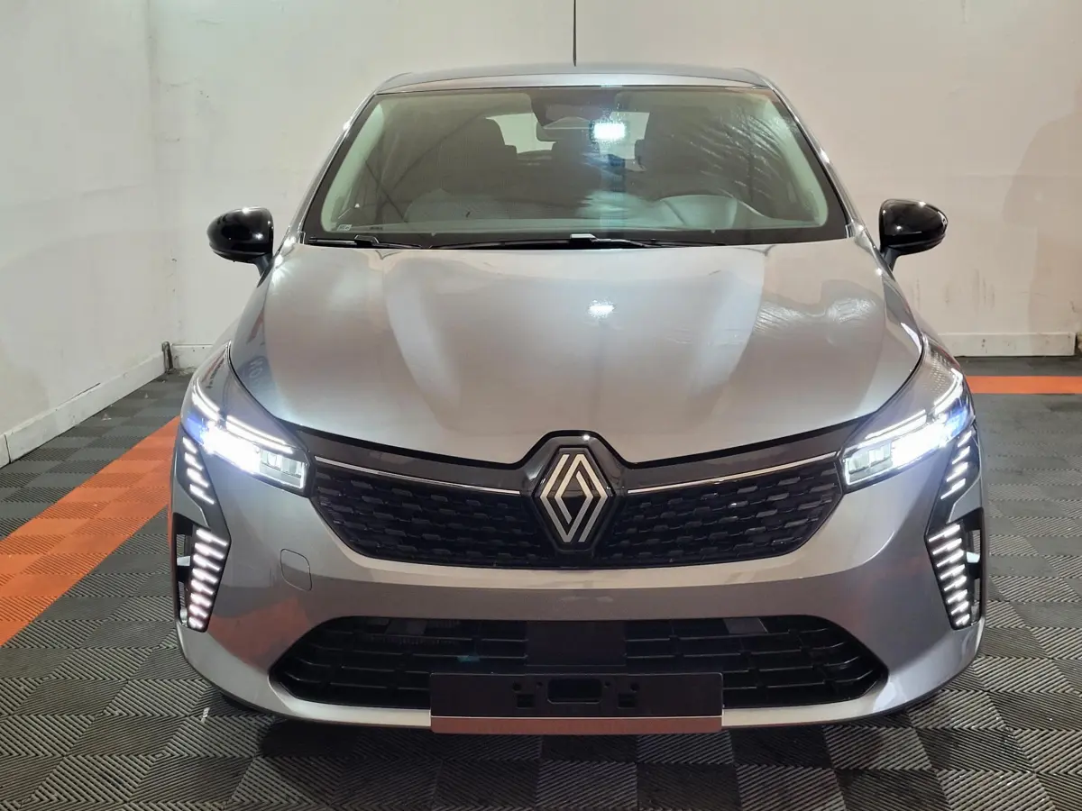 Vue avant d'une Renault Clio gris foncé 2025 avec phares LED allumés et calandre noire distinctive.