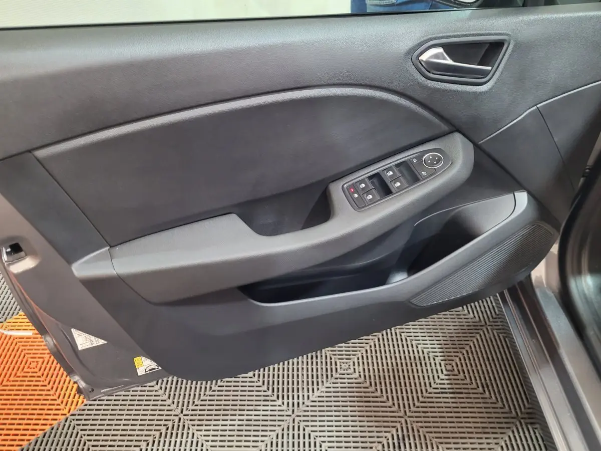 Vue intérieure côté gauche de la porte avant d'une Renault Clio gris foncé avec commandes électriques des vitres et poignée intégrée.