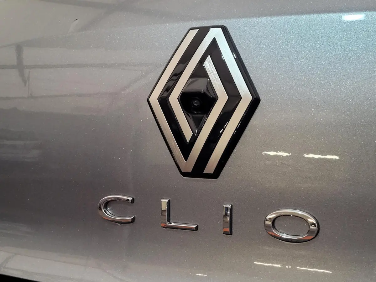 Gros plan sur le logo Renault et l’inscription Clio en chrome sur la carrosserie gris foncé métallisée.