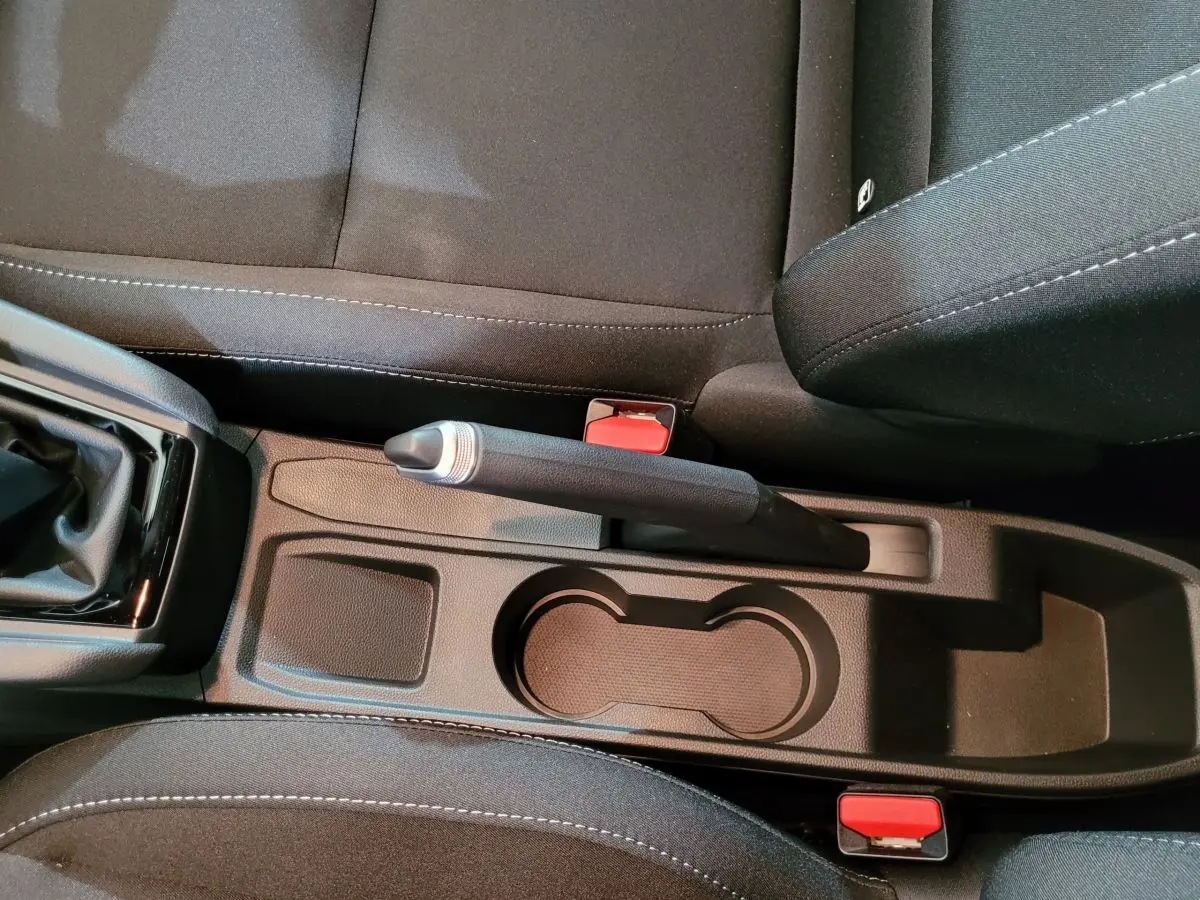 Vue rapprochée de la console centrale noire de la Renault Clio gris foncé, avec frein à main et porte-gobelets visibles.