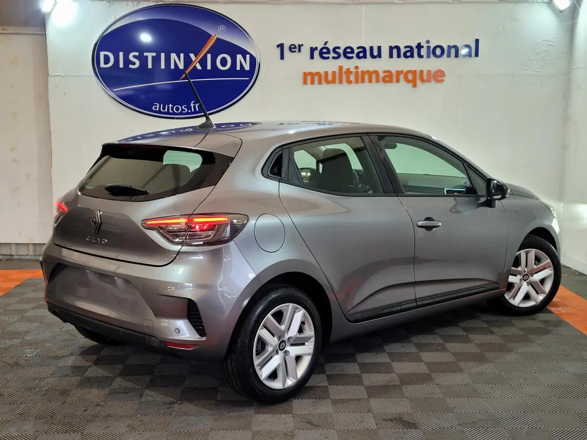 Renault Clio gris foncé vue 3/4 arrière droit, feux LED allumés, jantes alliage et antenne sur le toit.