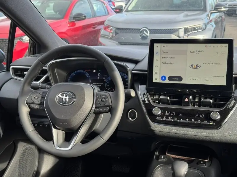 Vue intérieure centrée sur le volant cuir et l’écran tactile du tableau de bord de la Toyota Corolla noire 2025.