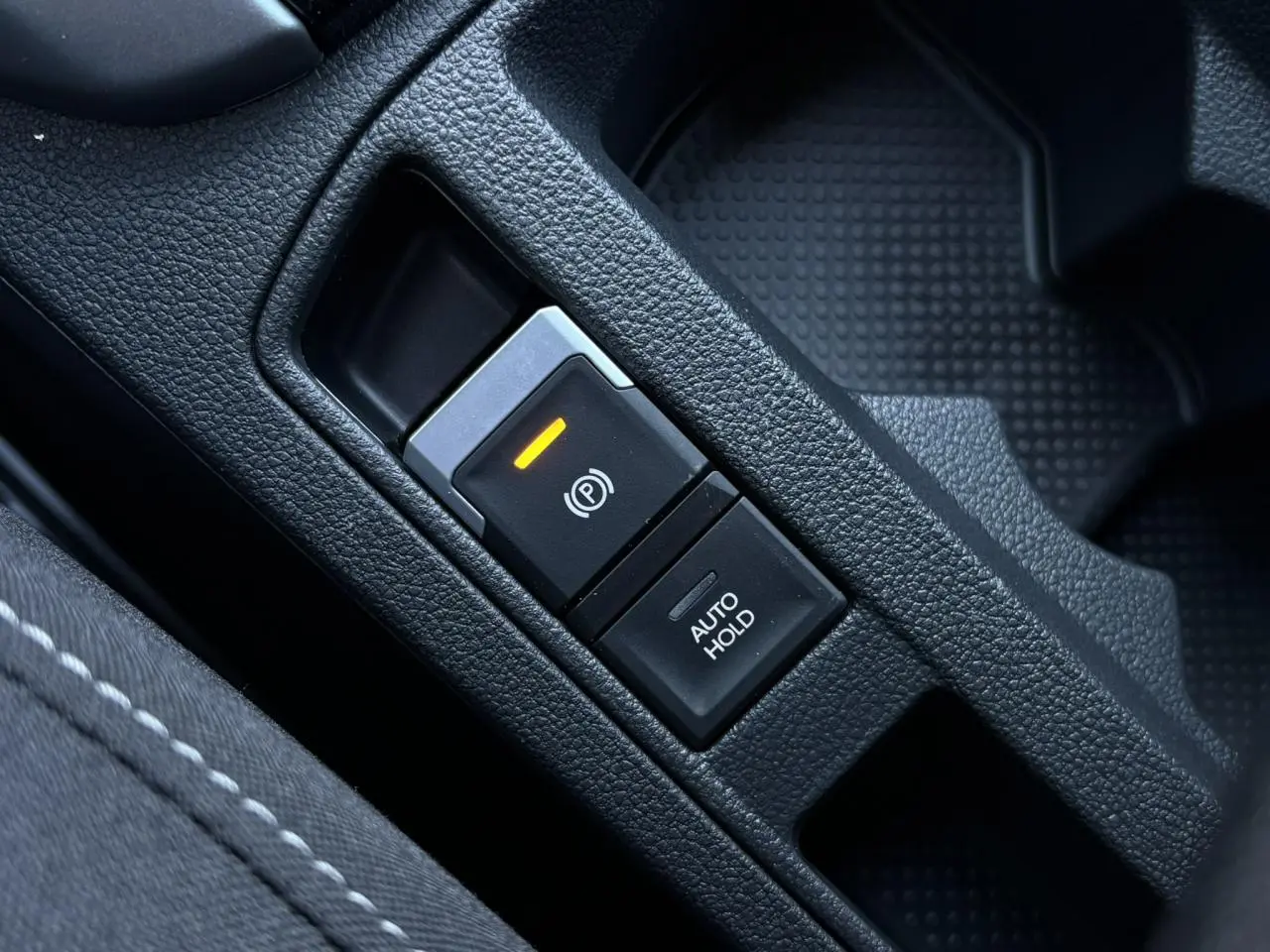 Gros plan sur le bouton de frein de stationnement électromécanique et fonction Auto-Hold dans un Volkswagen T-Roc gris Indium.