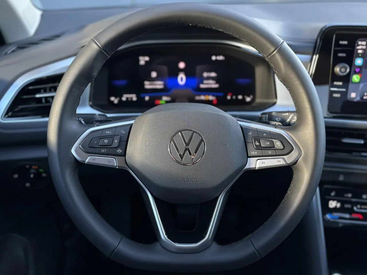 Vue rapprochée du volant en cuir multifonction noir du Volkswagen T-Roc 2025 avec tableau de bord digital en arrière-plan.