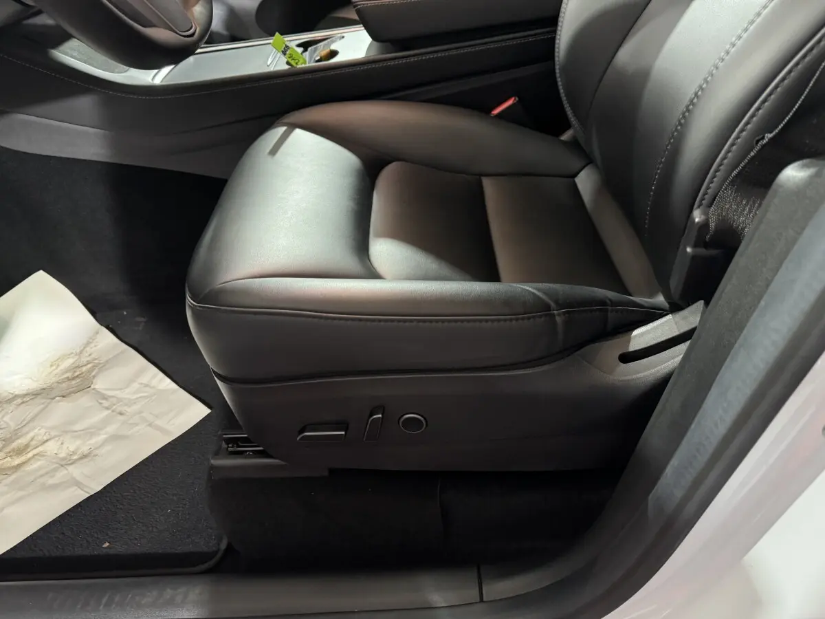Gros plan sur le siège avant droit en cuir noir du Tesla Model Y blanc, avec commandes électriques visibles.