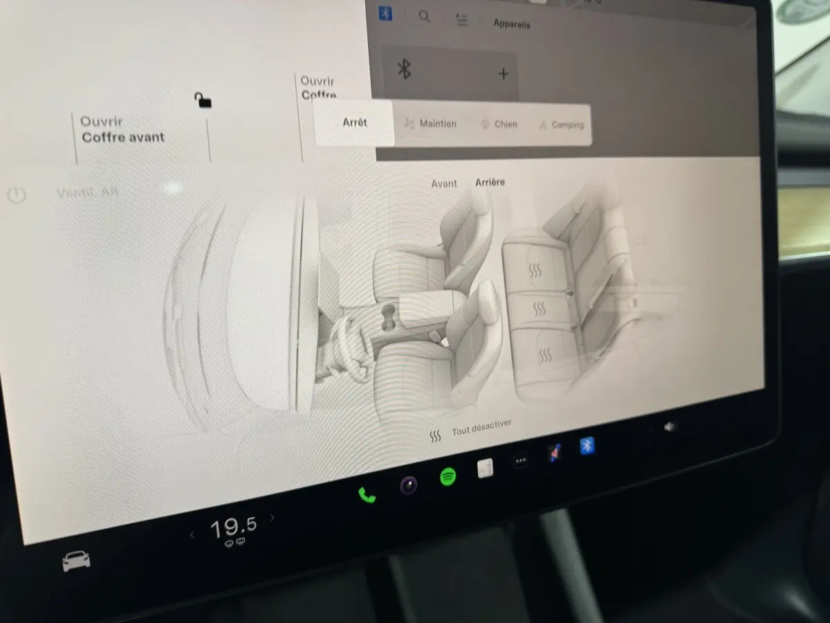 Écran tactile central affichant la configuration des sièges chauffants dans une Tesla Model Y blanche, vue intérieure.