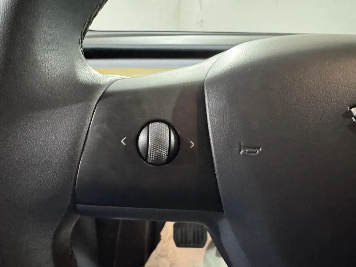 Gros plan sur la molette de réglage sur le côté gauche du volant noir d’un Tesla Model Y blanc.