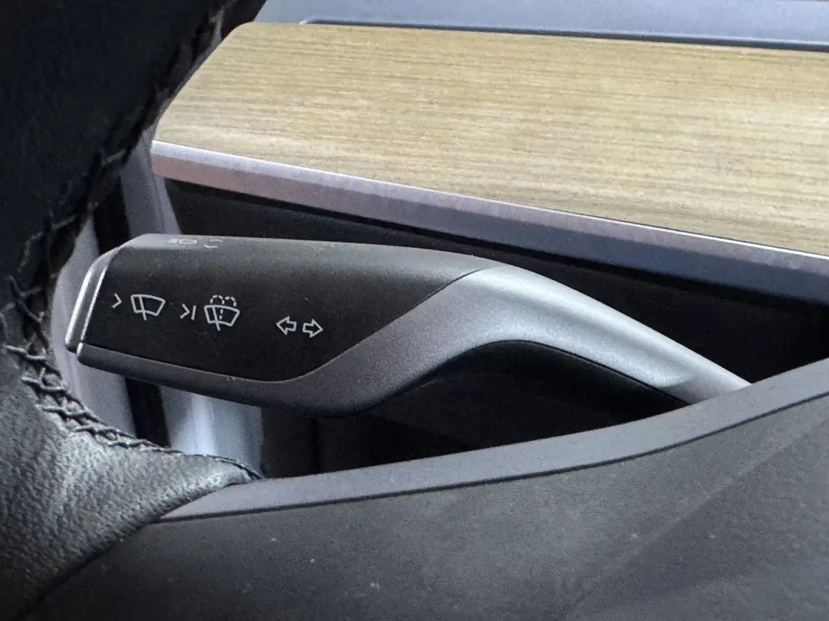 Gros plan sur la commande de clignotants et essuie-glaces noire dans l’habitacle du Tesla Model Y blanc.
