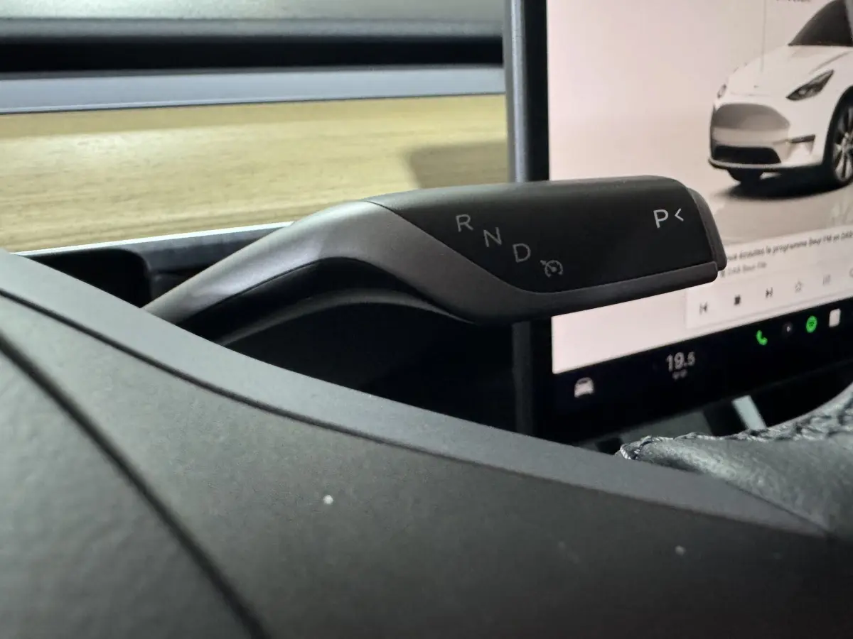 Gros plan sur la commande de boîte automatique à droite du volant dans le Tesla Model Y blanc, avec écran tactile en arrière-plan.