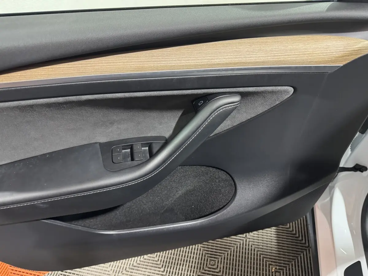 Vue rapprochée de la porte avant gauche blanche d’un Tesla Model Y 2022 avec garniture bois et commandes électriques.