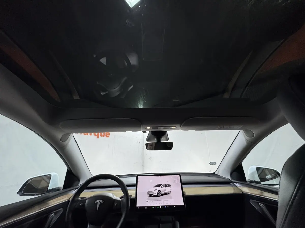 Vue intérieure frontale du Tesla Model Y blanc 2022, avec grand écran tactile central et toit panoramique.