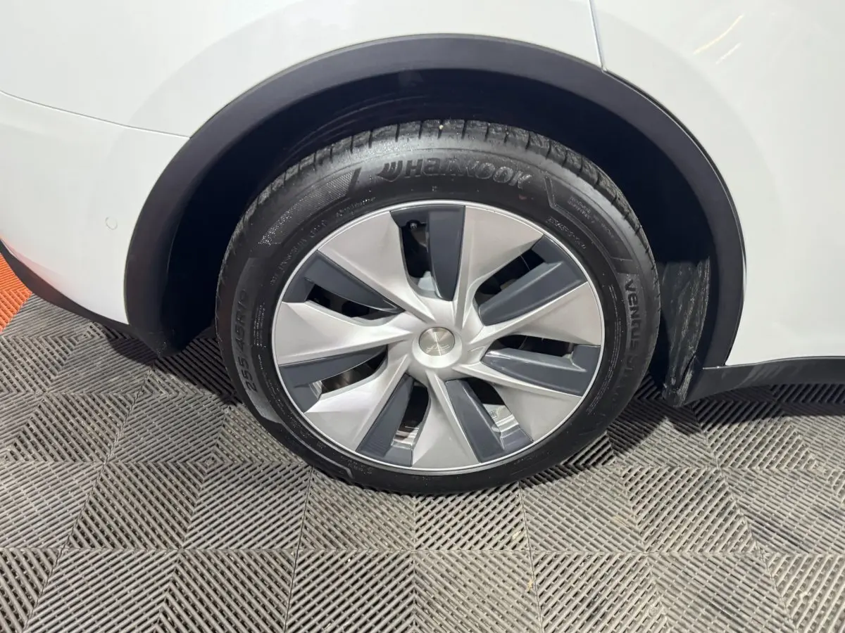 Gros plan sur la roue arrière droite d’un Tesla Model Y blanc, mettant en valeur la jante aérodynamique et le pneu Hankook.