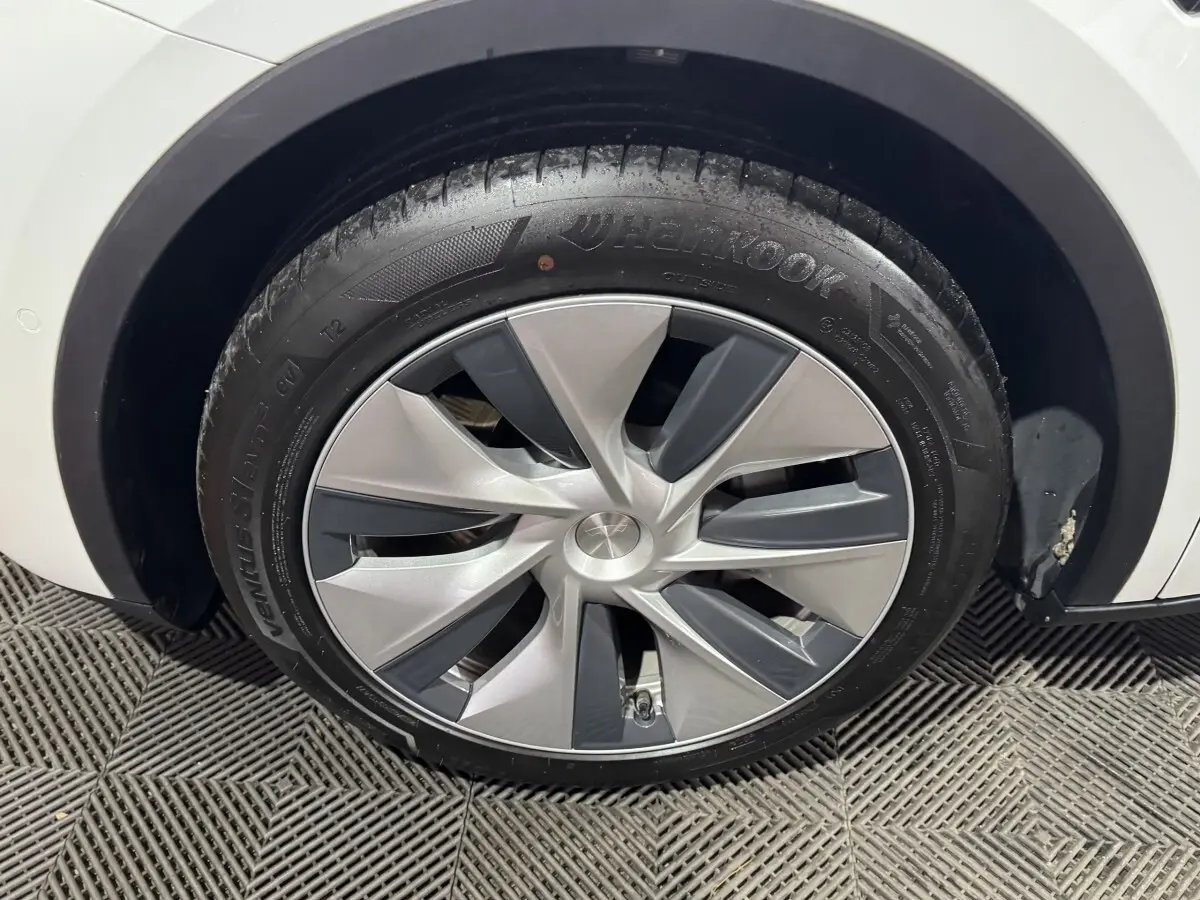 Gros plan sur la roue avant droite d’un Tesla Model Y blanc avec jante aérodynamique grise et noire.
