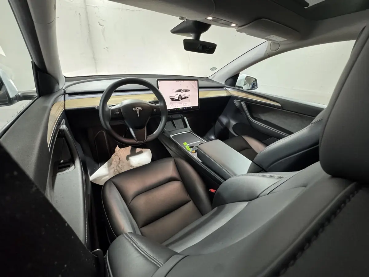 Intérieur Tesla Model Y blanc vu côté passager avant, tableau de bord épuré avec écran tactile central et sièges cuir noirs.
