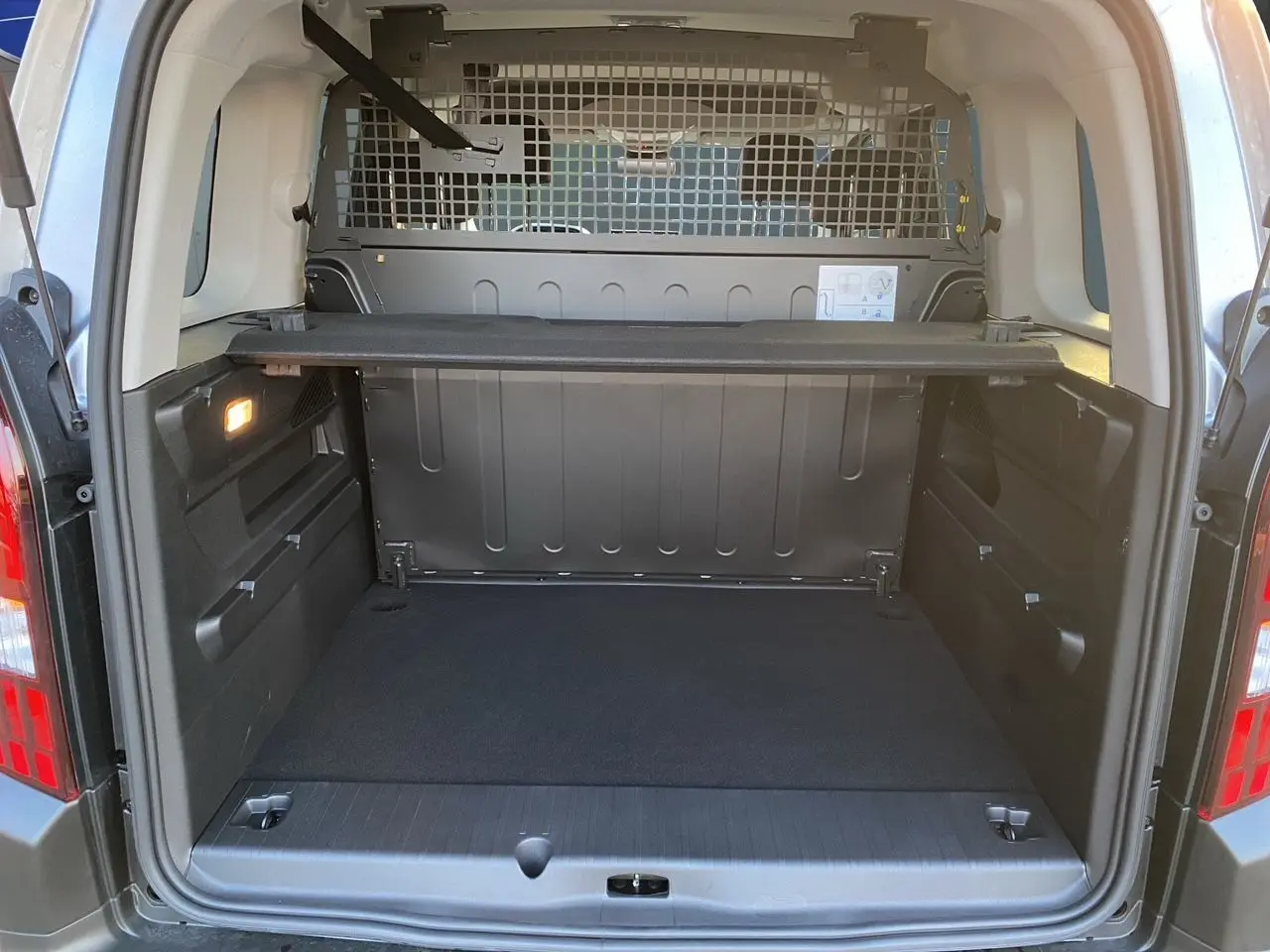 Coffre ouvert du Peugeot Rifter gris acier, vue arrière montrant la cloison métallique et le cache-bagages.