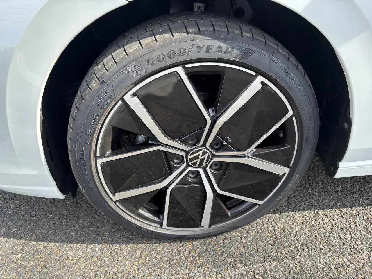 Gros plan sur la roue avant droite d'une Volkswagen Golf blanche 2024 avec jante noire et argentée au design moderne.