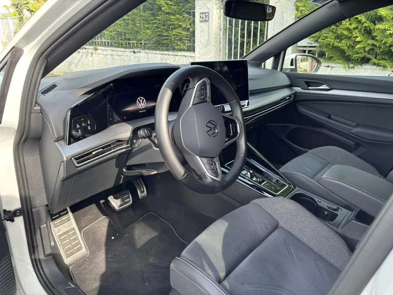 Vue intérieure côté conducteur de la Volkswagen Golf blanche 2024, avec tableau de bord numérique et volant multifonction.