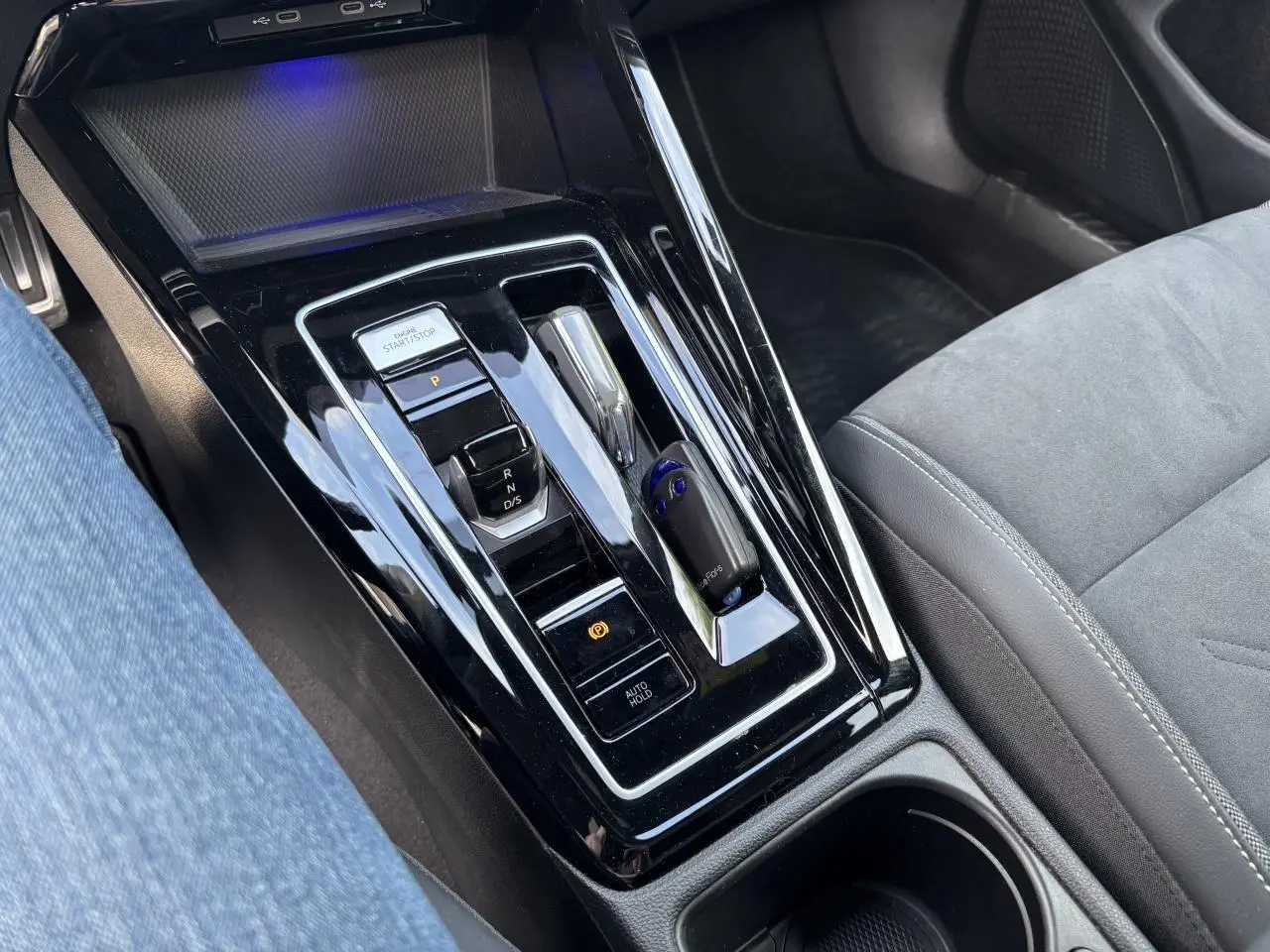 Vue rapprochée de la console centrale noire brillante de la Volkswagen Golf 1.5 eTSI 2024 avec levier de vitesse automatique et bouton start/stop.