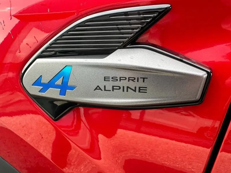 Gros plan sur l'emblème Esprit Alpine bleu et noir sur la carrosserie Rouge Flamme du Renault Captur 2025.