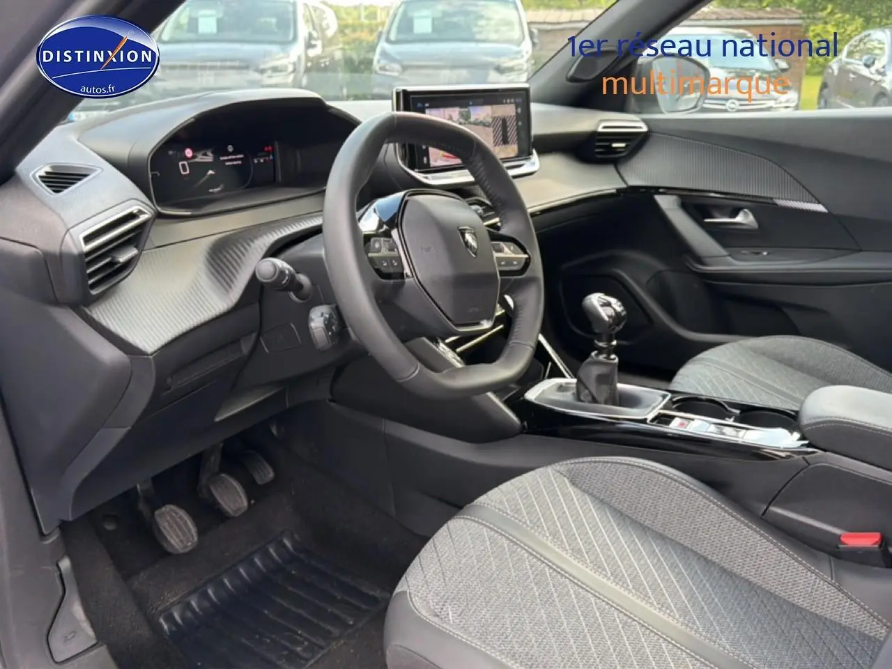 Vue intérieure côté conducteur du Peugeot 2008 1.2 100 allure 2025 avec volant multifonction et sellerie tissu gris.