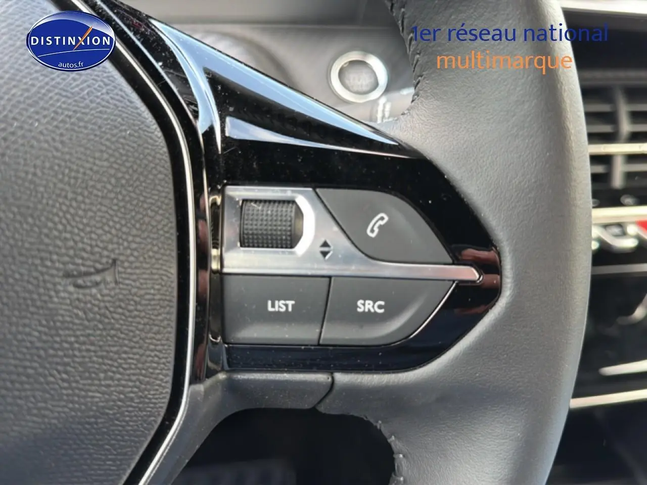 Gros plan sur les commandes gauche du volant noir du Peugeot 2008 gris artense, avec boutons multifonctions et molette.