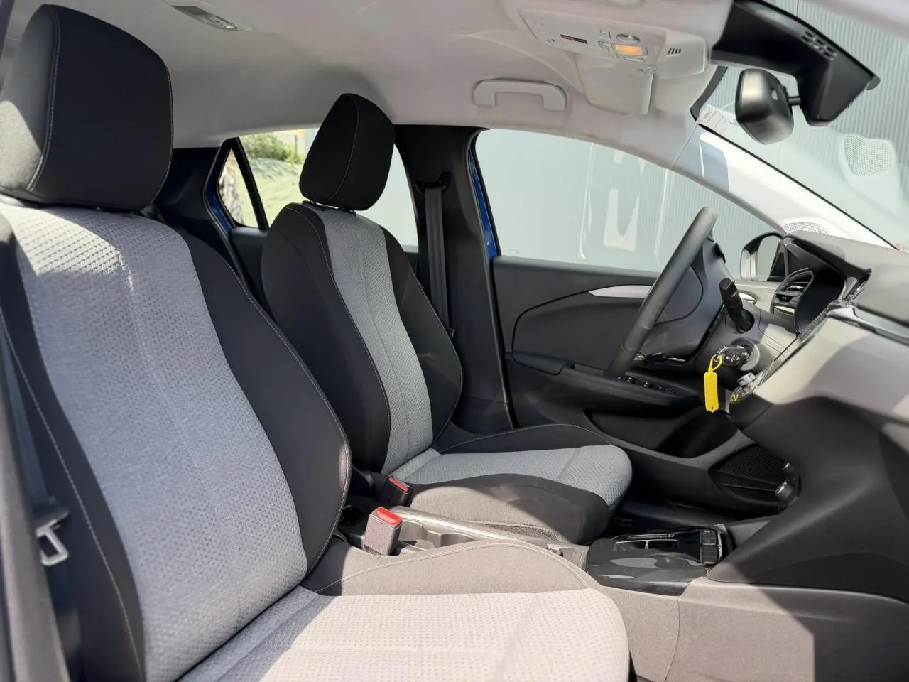 Vue intérieure côté gauche de l’Opel Corsa 2025 bleu Voltaic, montrant les sièges avant bicolores et le tableau de bord moderne.