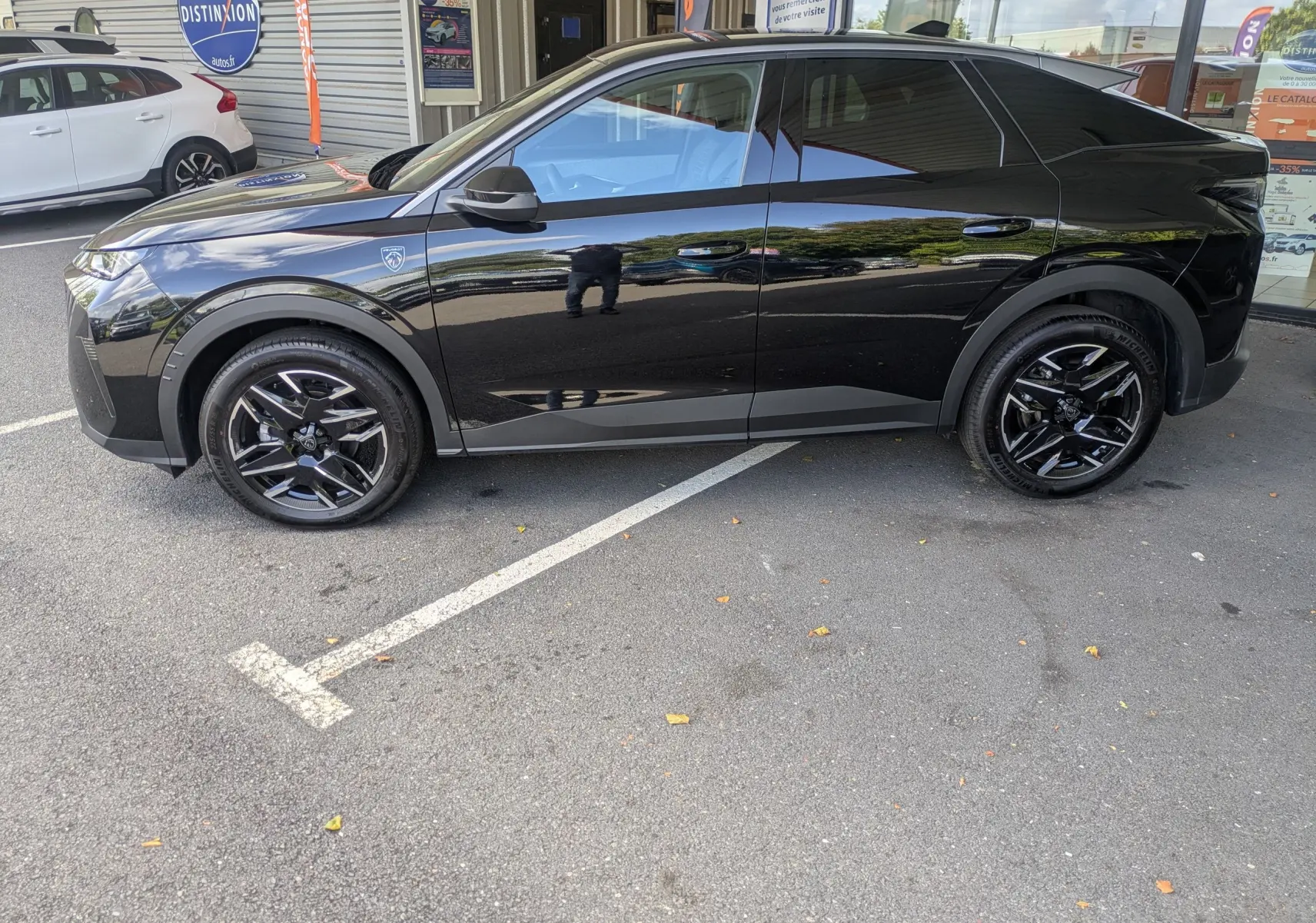 Profil côté gauche du Peugeot 3008 Hybrid 145 GT noir brillant avec jantes noires et vitres teintées, stationné devant un bâtiment.