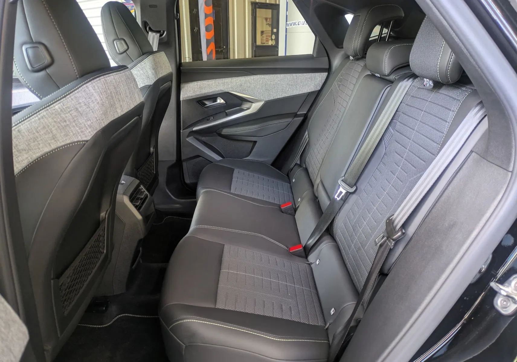 Vue intérieure côté droit des sièges arrière du Peugeot 3008 Hybrid 145 GT noir avec sellerie tissu embossée et surpiqûres claires.